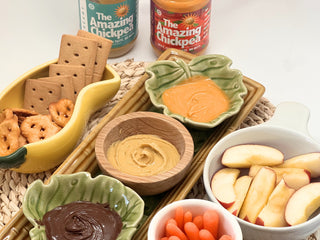 An arrangement of dipping bowls with chickpea butters, crackers, and fruit with jars labeled 'The Amazing Chickpea'