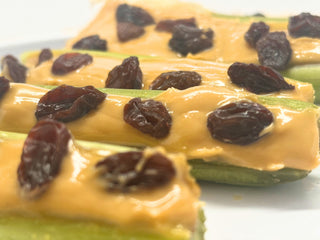 Close-up of celery sticks filled with chickpea butter and raisins on a white background