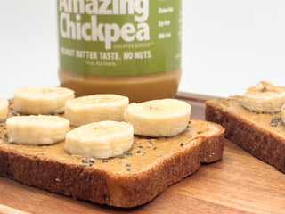 Two slices of chickpea butter and banana toast on a cutting board beside a jar of The Amazing Chickpea