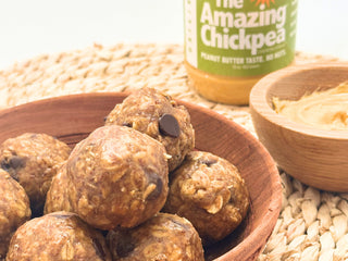 Bowl of protein balls with a jar labeled 'The Amazing Chickpea' and a small bowl of creamy chickpea butter beside it