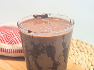 Glass of chocolate smoothie on a cutting board beside a red tea towel