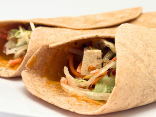 Close-up of two rolled up veggie, tofu, and chickpea butter wraps on a white background
